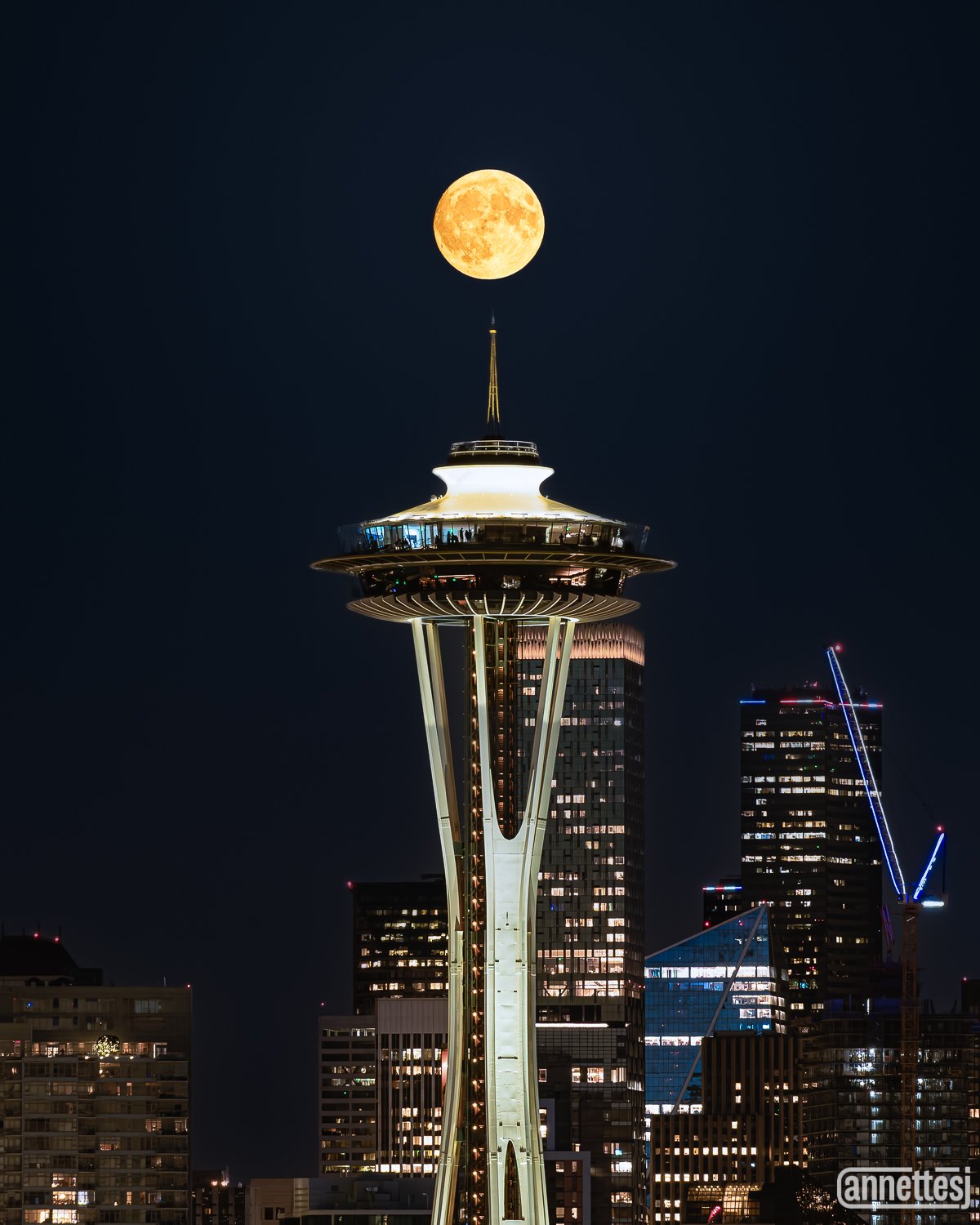 A full moon over the Seattle skyline with the Space Needle illuminated at night.